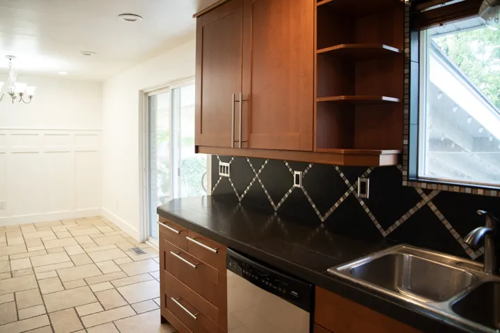 Wood-finish cabinetry with silver-tone hardware, dark countertop, and a stainless steel sink