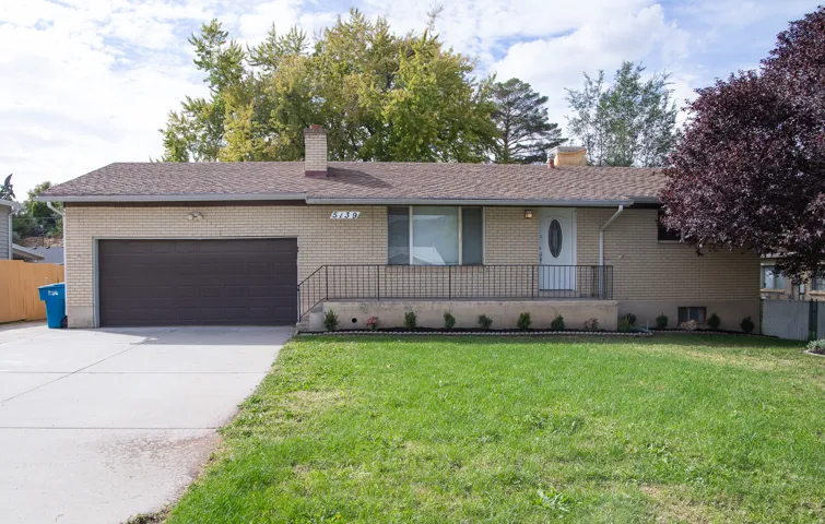 Brick exterior, attached garage, concrete driveway, front porch with metal railing, and mature landscaping