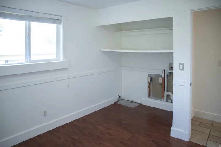 Wood-finish flooring, built-in shelving, white trim, and a window with blinds
