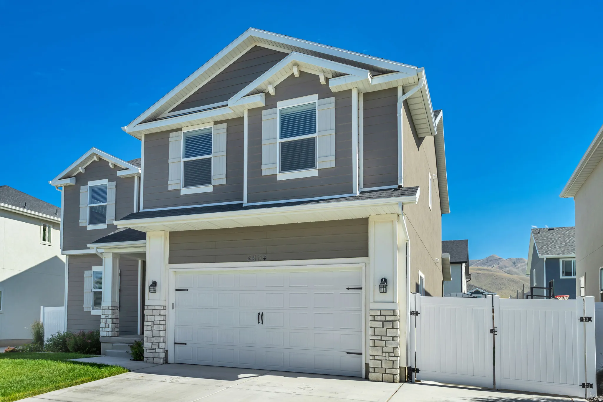 Two-story residence featuring grey siding, white trim, a two-car garage, and a white privacy fence