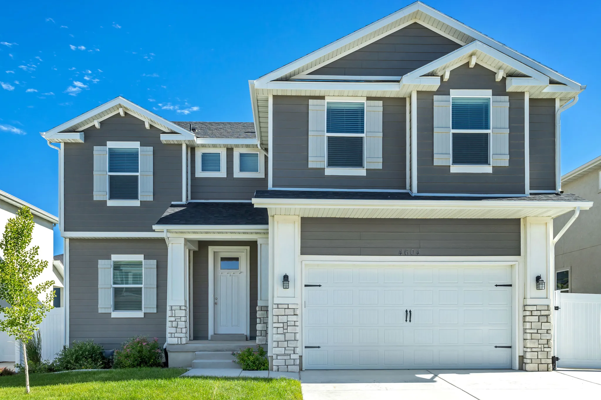 Two-story exterior with dark gray siding, white window shutters, two-car garage, and stone veneer accents
