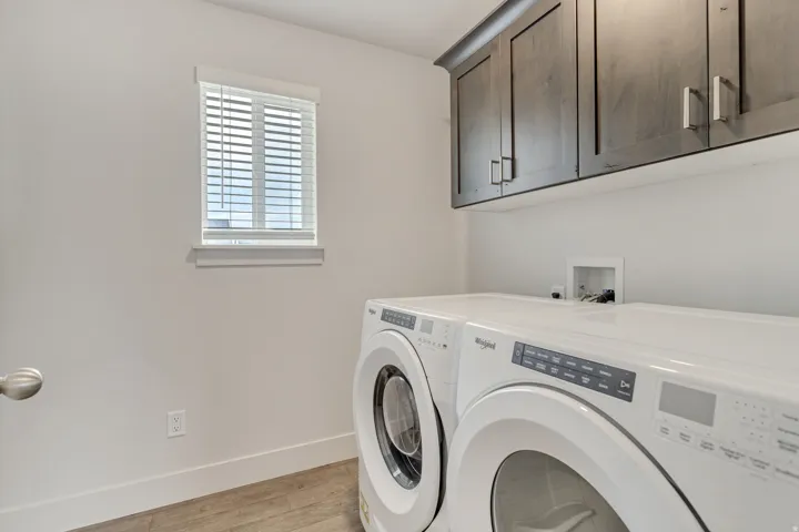 Laundry area featuring wood-finish flooring, a window with blinds, and built-in upper cabinetry with modern hardware