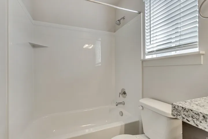 Bathtub with integrated shelving, chrome shower fixtures, and a window with blinds