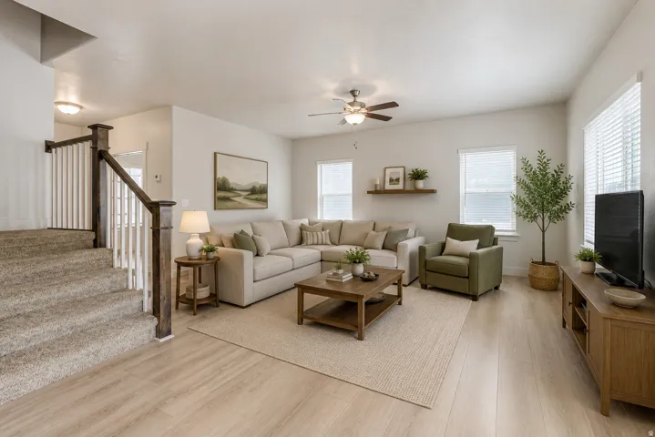 Spacious living area featuring light wood-finish flooring, a contemporary ceiling fan, multiple windows with blinds, and a built-in wall shelf