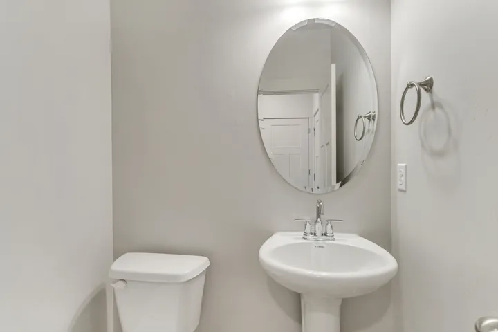White pedestal sink with chrome faucet, oval mirror, and white toilet