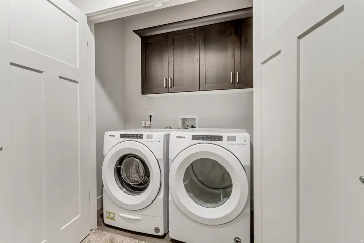 Laundry area featuring dark wood-finish cabinetry with silver hardware, white walls, and bi-fold doors