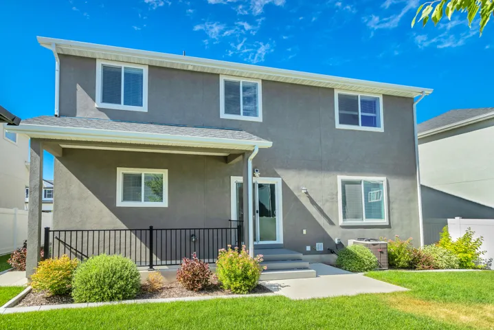 Stucco exterior with multiple windows, covered patio featuring a black metal railing, and concrete steps leading to the lawn