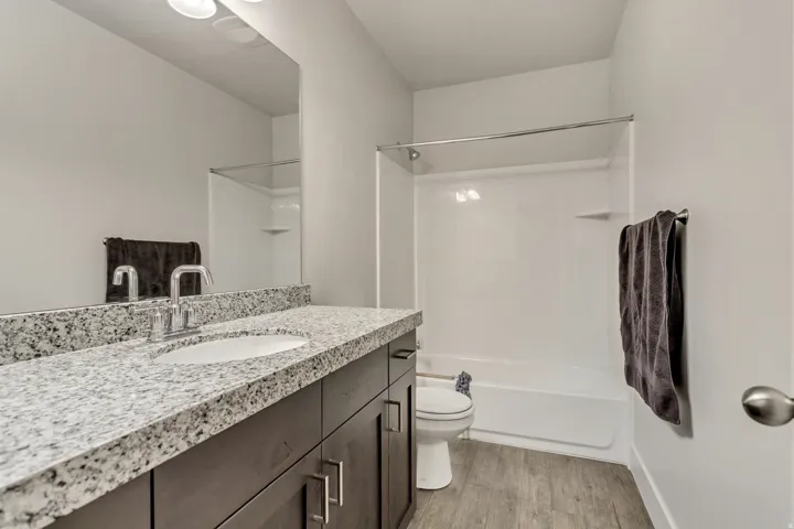 Bathroom featuring a granite-finish countertop, undermount sink, dark wood-finish vanity with cabinet storage, and a shower-tub combination with a chrome shower rod