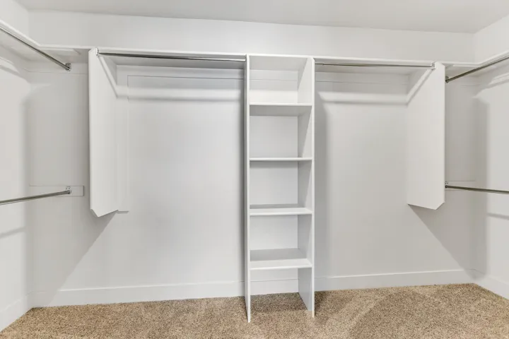 Built-in shelving unit with five tiers, multiple hanging rods, and carpet flooring