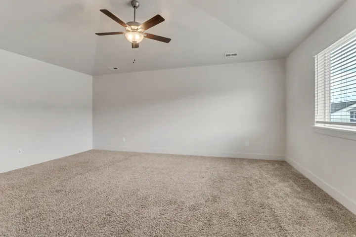 Neutral tone carpeting, light-colored walls, window with blinds, and a ceiling fan with integrated lighting