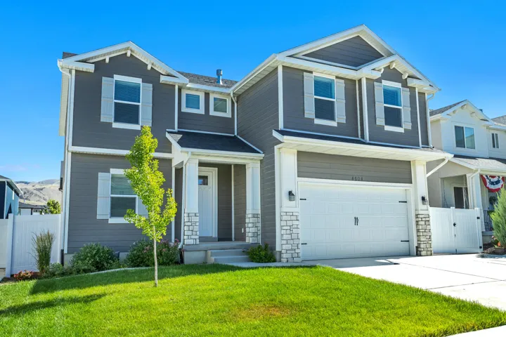 Two-story exterior with gray siding, white trim, attached two-car garage, covered entry, and stone accents
