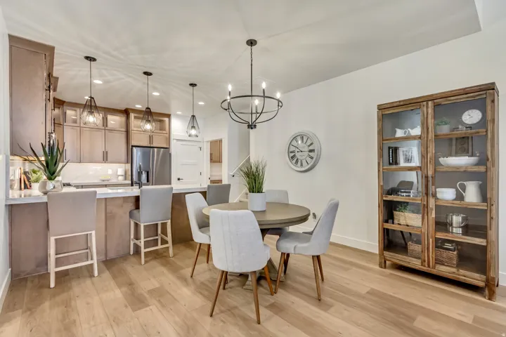 Kitchen with breakfast bar, stainless steel refrigerator, and pendant lighting, adjacent to dining area with wood-finish flooring and contemporary chandelier