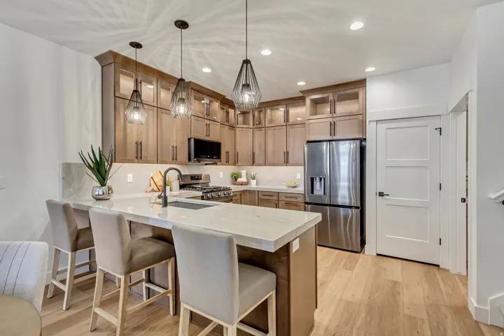 Kitchen featuring wood-finish cabinetry, stainless steel appliances, a white stone countertop island with a sink, pendant lighting, and wood-finish flooring