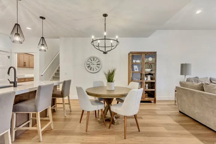 Open-concept living space featuring light wood-finish flooring, a kitchen island with seating, a dedicated dining area, and a staircase