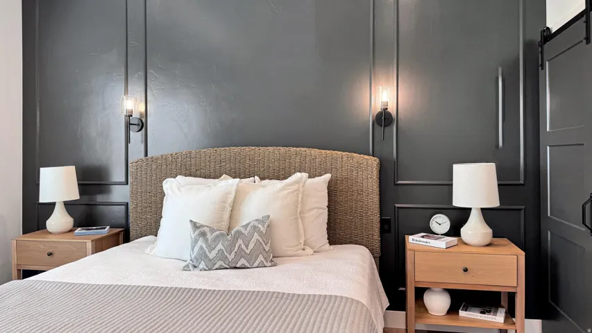 Accent wall with panel molding, integrated wall sconces, woven headboard, wood-finish nightstands, and a built-in barn door