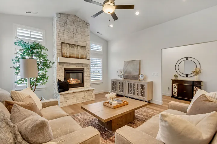 Stone-clad fireplace with mantel, vaulted ceiling with ceiling fan, wood-finish flooring, and plantation shutters