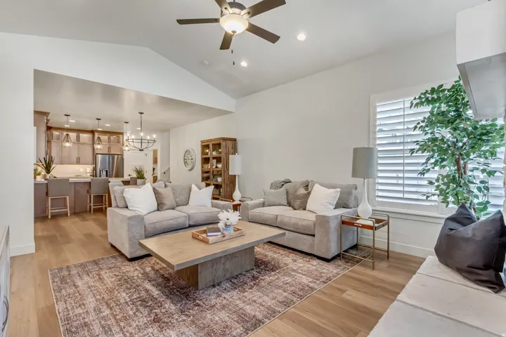 Vaulted ceilings, wood-finish flooring, kitchen with built-in cabinetry and stainless steel appliances, ceiling fan, and window with plantation shutters