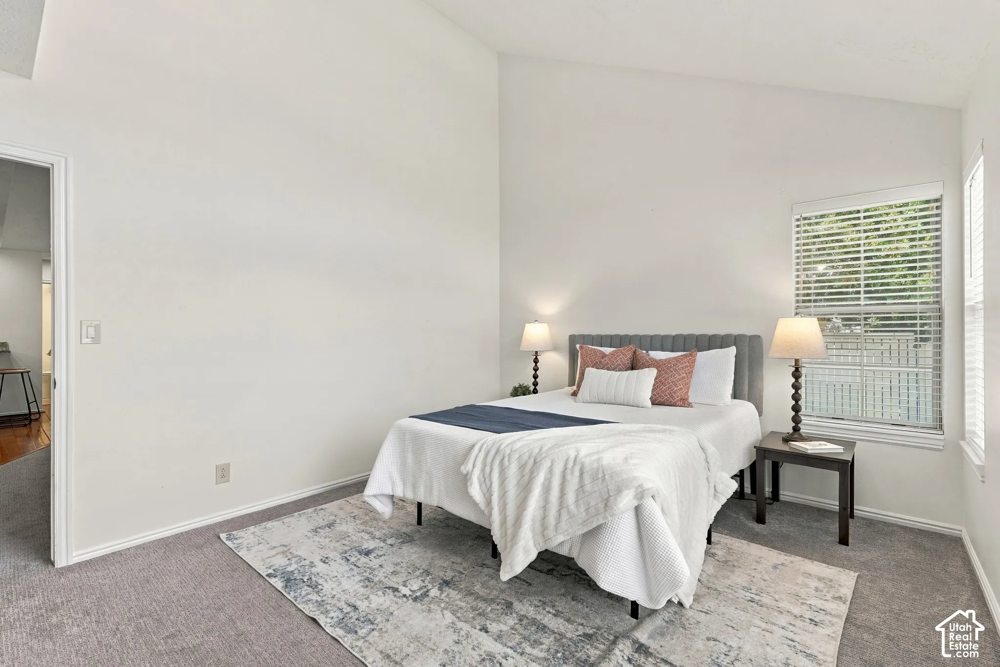 Vaulted ceiling, carpeted flooring, window with blinds, and white painted walls