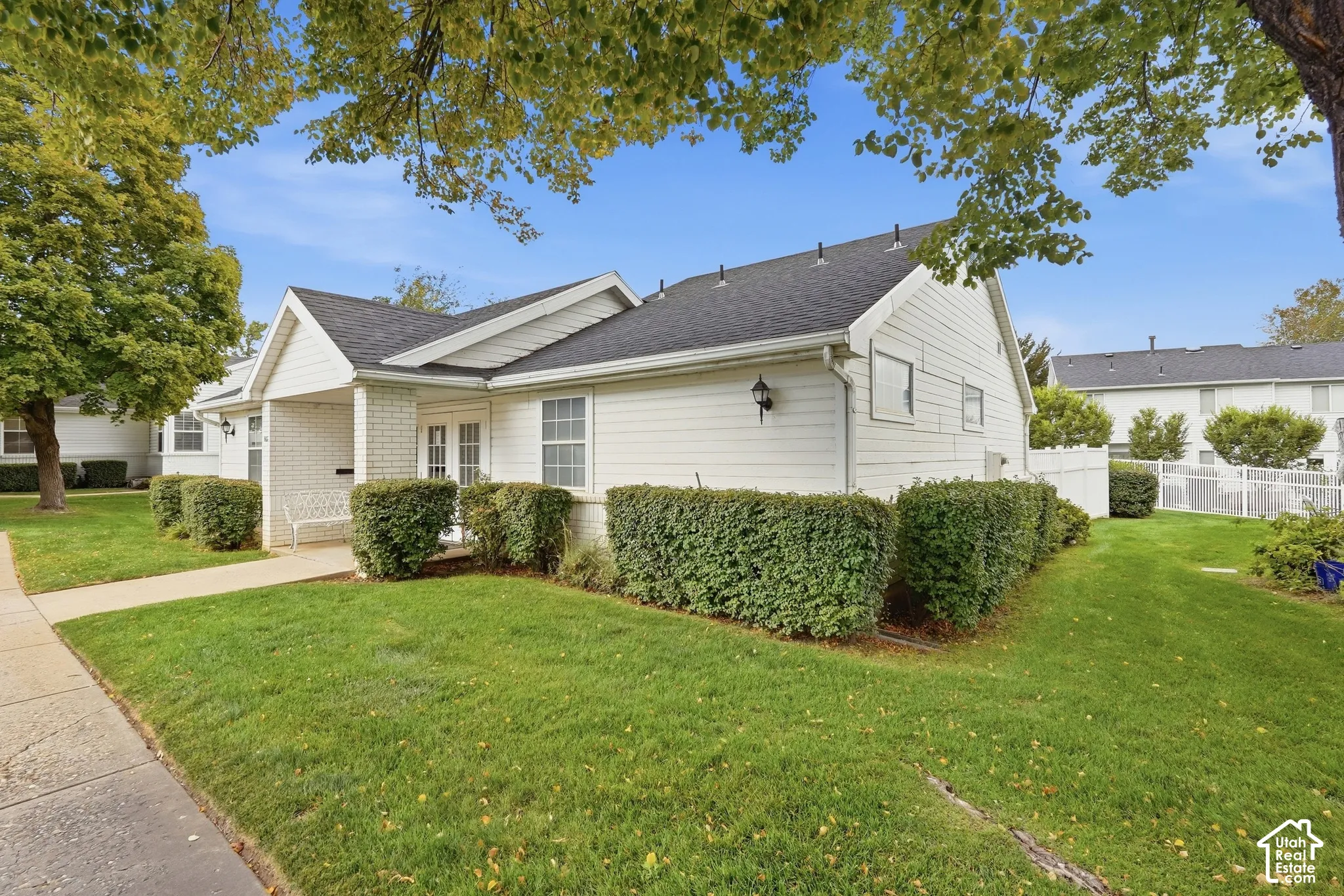 White siding exterior with a brick accent entry, dual front windows, and a paved walkway