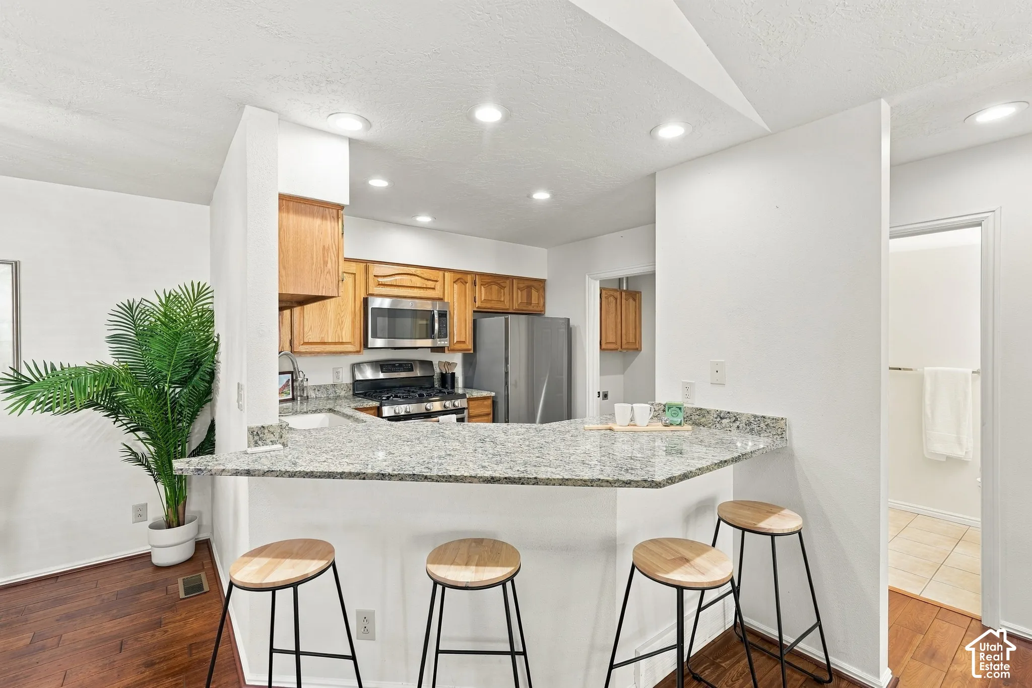 Kitchen featuring wood cabinetry, stainless steel appliances, recessed lighting, and a breakfast bar with stone-finish countertops