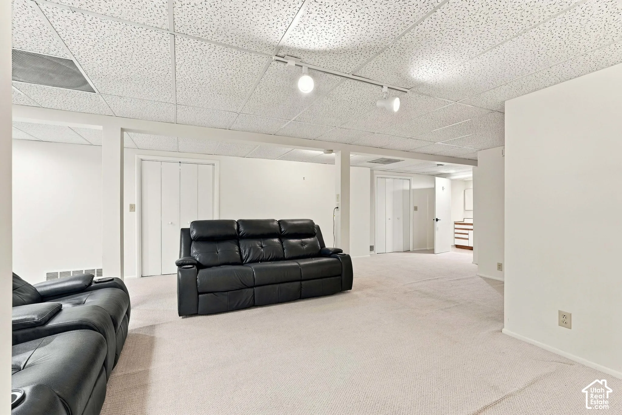 Carpeted flooring, acoustic panel ceiling, track lighting, and white bi-fold doors