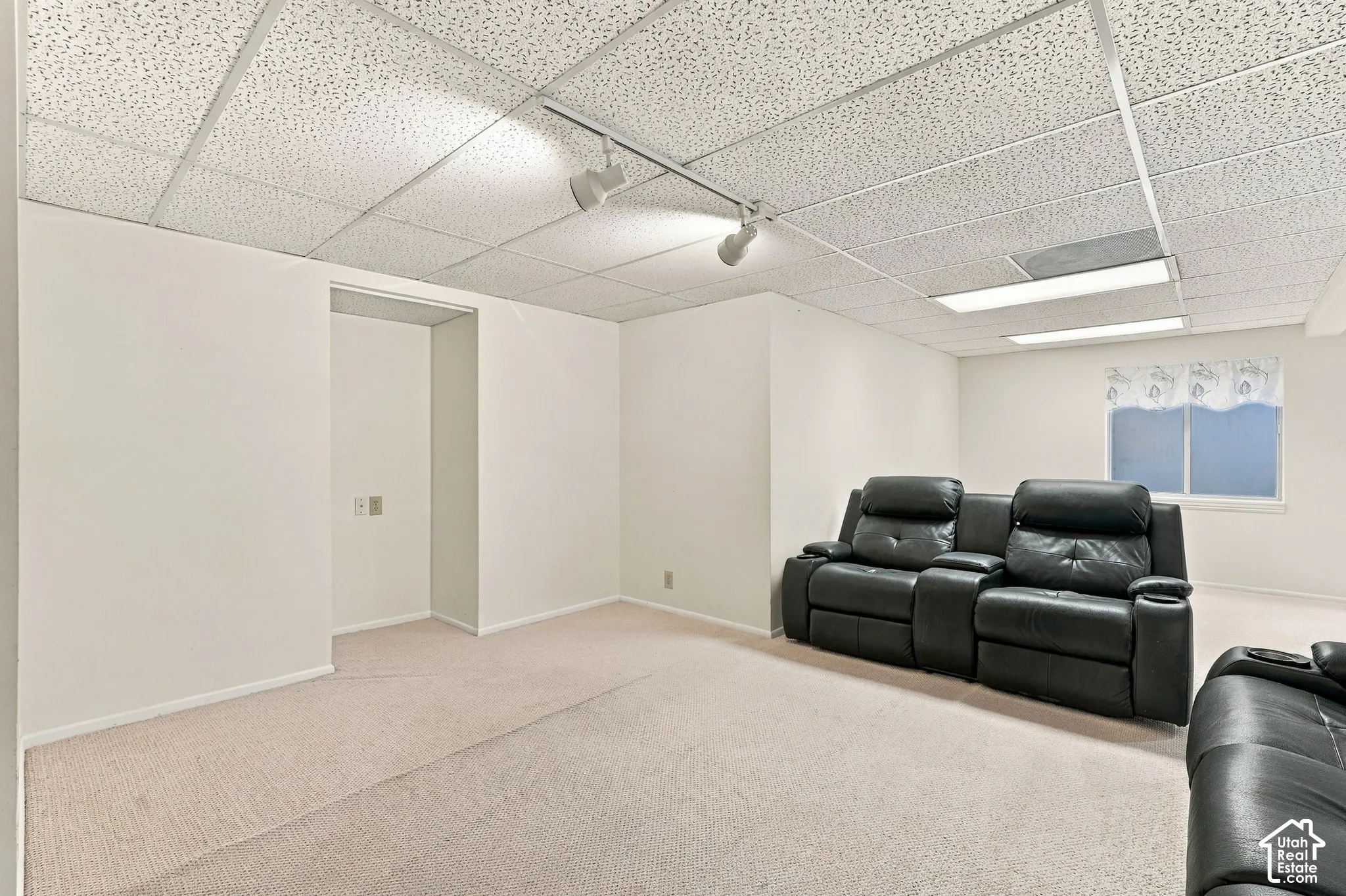 Recessed lighting, track lighting, and drop ceiling panels illuminate this carpeted room with an open doorway