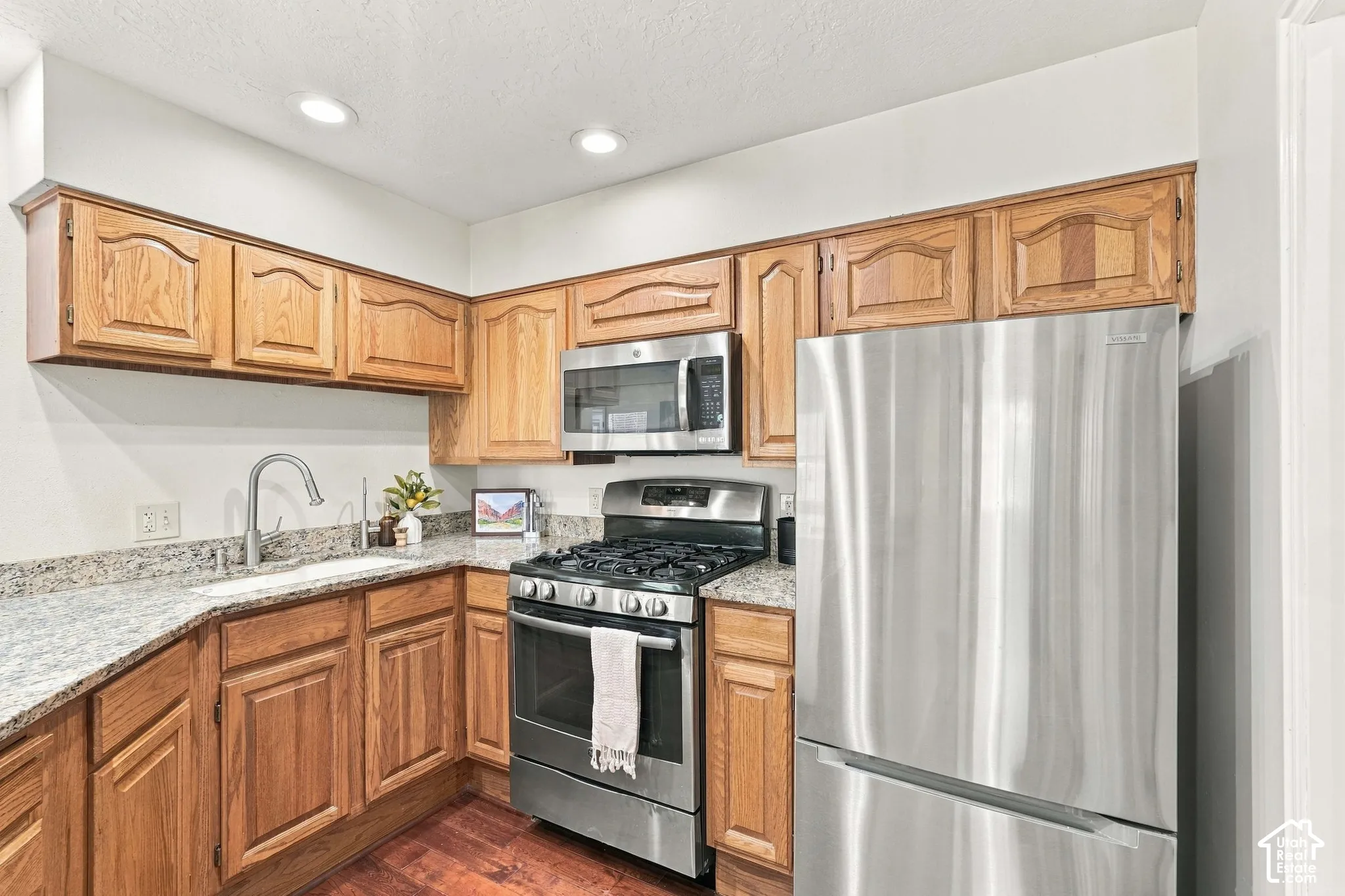 Kitchen featuring wood-finish cabinetry, stainless steel appliances, granite countertops, an undermount sink, and recessed lighting