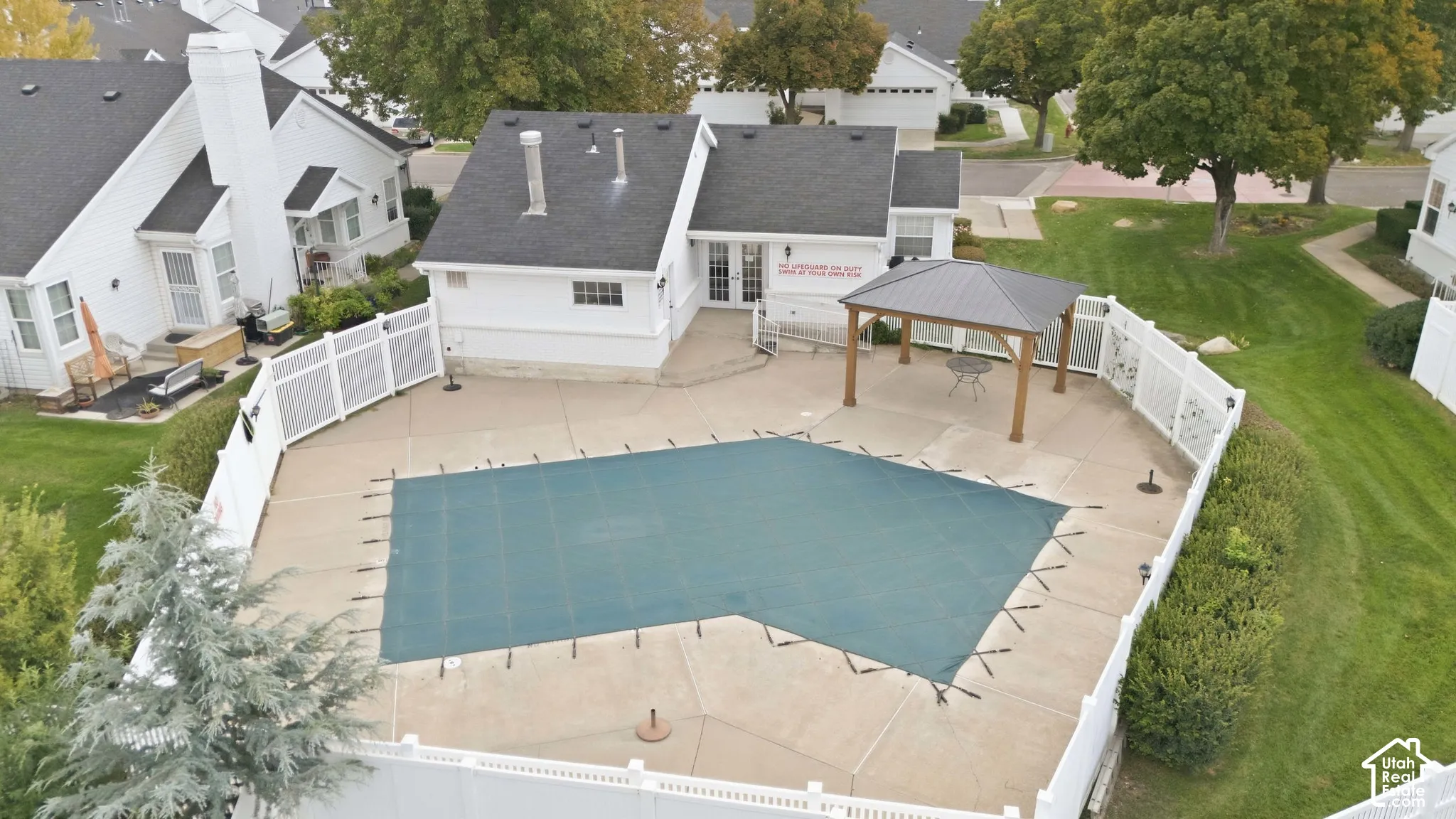 Fenced outdoor pool area with a covered pool and surrounding concrete patio