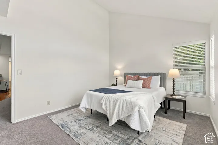 Vaulted ceiling, carpeted flooring, window with blinds, and white painted walls