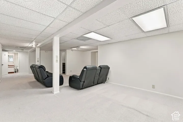 Carpeted room featuring a drop ceiling with integrated lighting, white walls, and structural columns