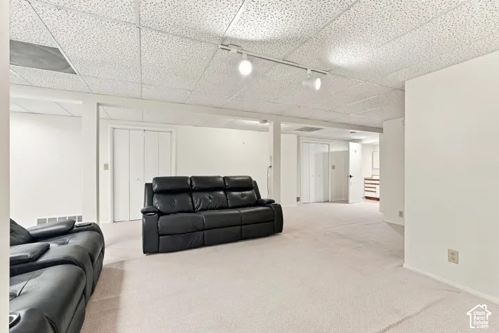 Carpeted flooring, acoustic panel ceiling, track lighting, and white bi-fold doors