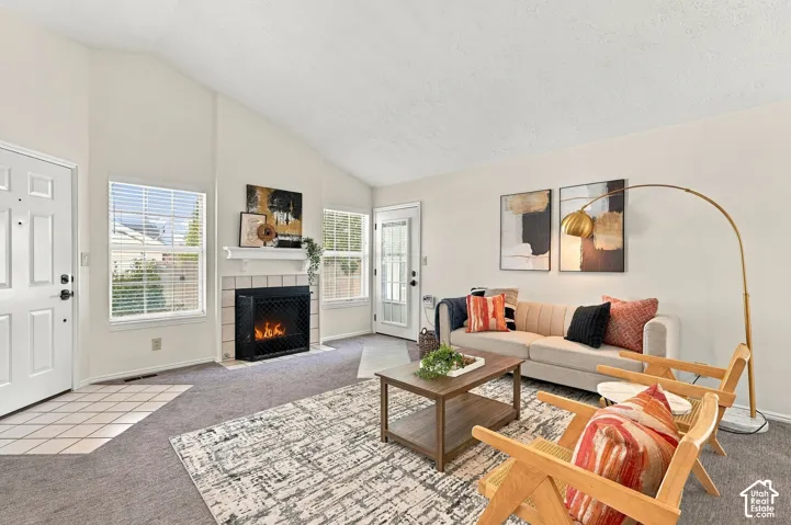 Living area with vaulted ceilings, a fireplace with a tiled surround, and multiple windows