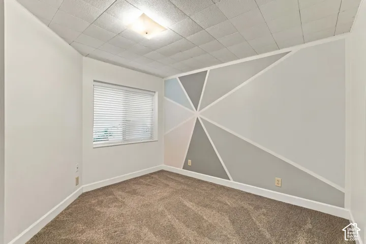 Geometric accent wall, window with blinds, overhead lighting fixture, and carpet flooring