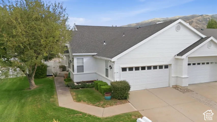 White siding exterior with a dark shingle roof, attached garage, and mountain backdrop