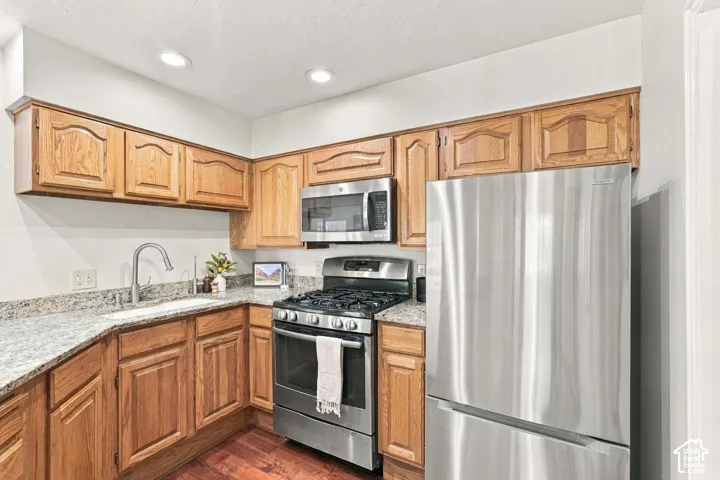 Kitchen featuring wood-finish cabinetry, stainless steel appliances, granite countertops, an undermount sink, and recessed lighting