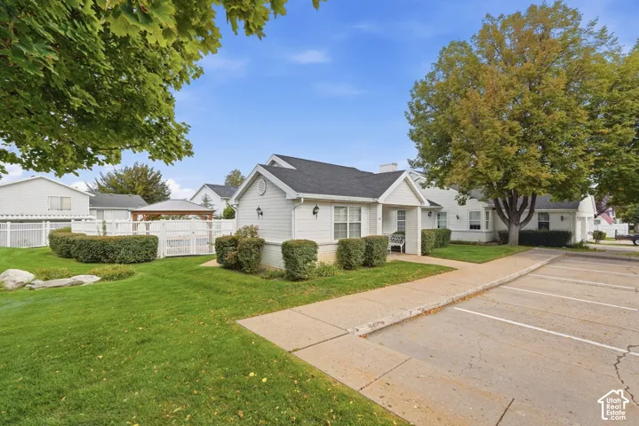 White siding exterior with a dark shingle roof, established landscaping, and a paved parking area