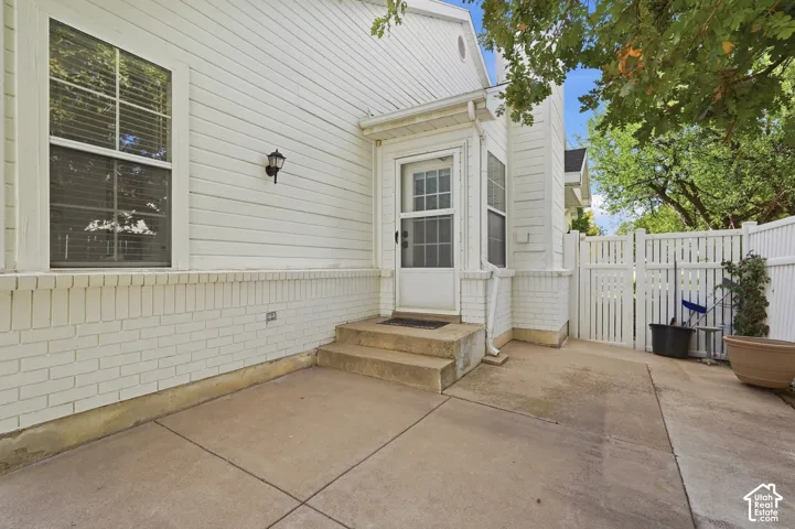 Exterior featuring white siding, a white brick foundation, concrete patio space, a white privacy fence, and an exterior wall lantern