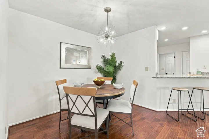 Hardwood-style flooring throughout, modern Sputnik-style light fixture, white walls, and a breakfast bar with stone-finish countertops
