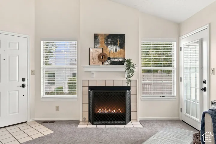 Vaulted ceiling, white paneled entry door, tiled fireplace hearth, white tile fireplace surround, and a glass-paneled patio door