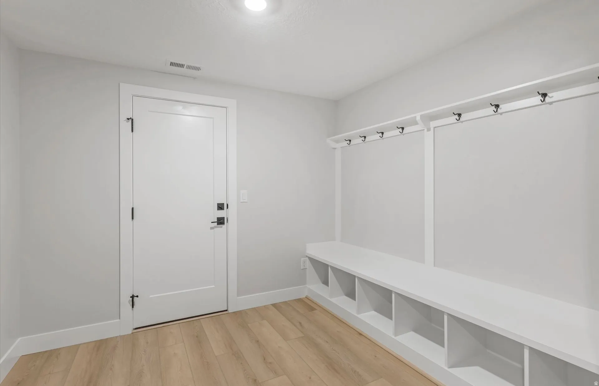Built-in bench seating with cubby storage, integrated coat rack with hooks, wood-finish flooring, and a flush-mounted ceiling light