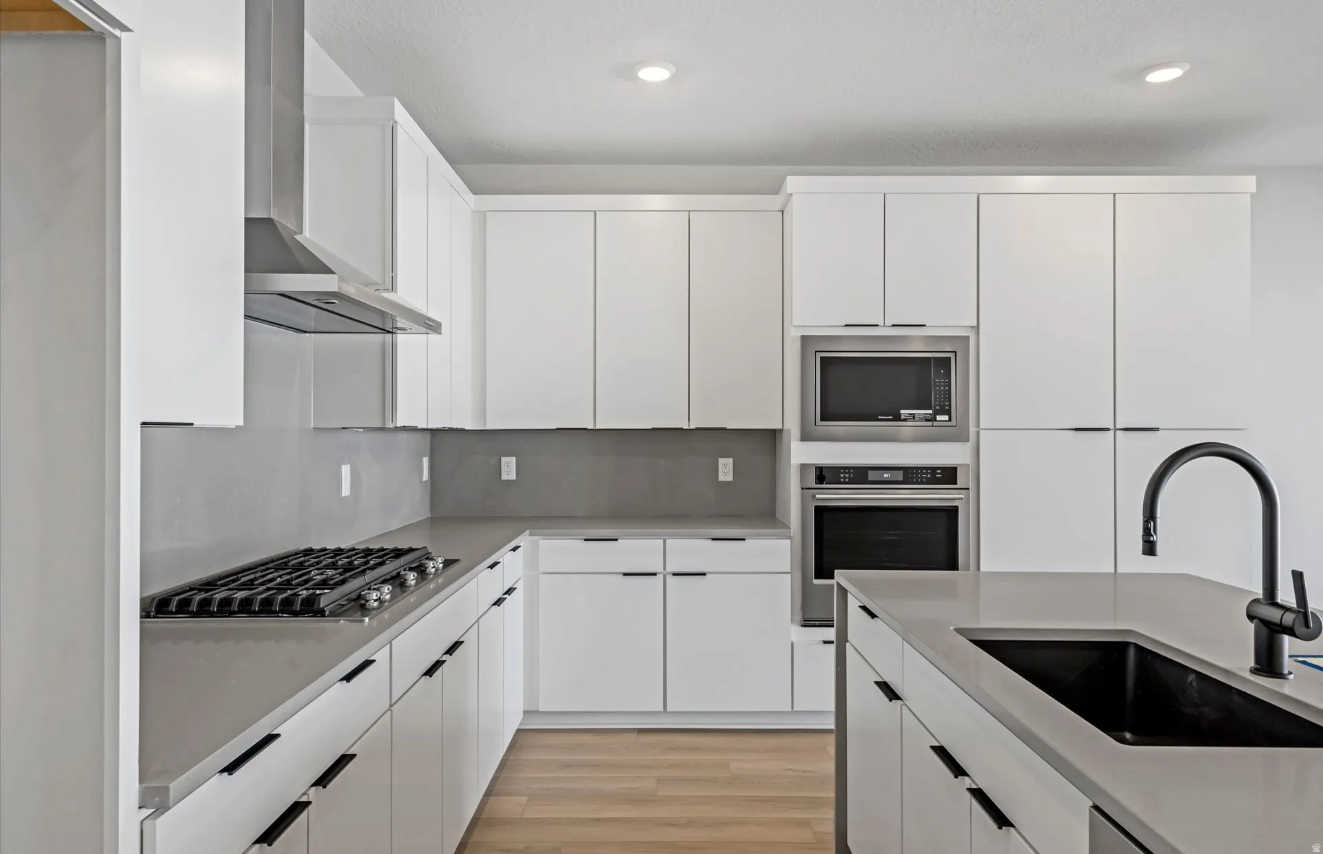 White cabinetry, stainless steel appliances, kitchen island with black sink, light wood-finish flooring, and recessed lighting