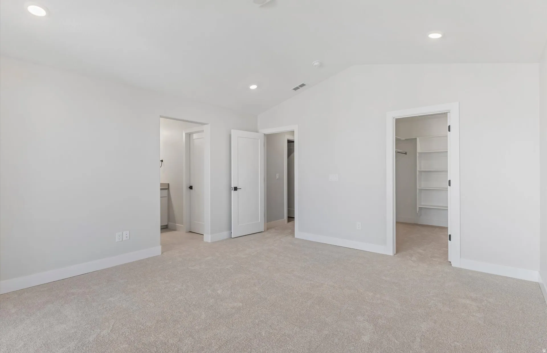 Recessed lighting, vaulted ceiling, light-toned carpeting, built-in closet shelving, and a vanity with a countertop