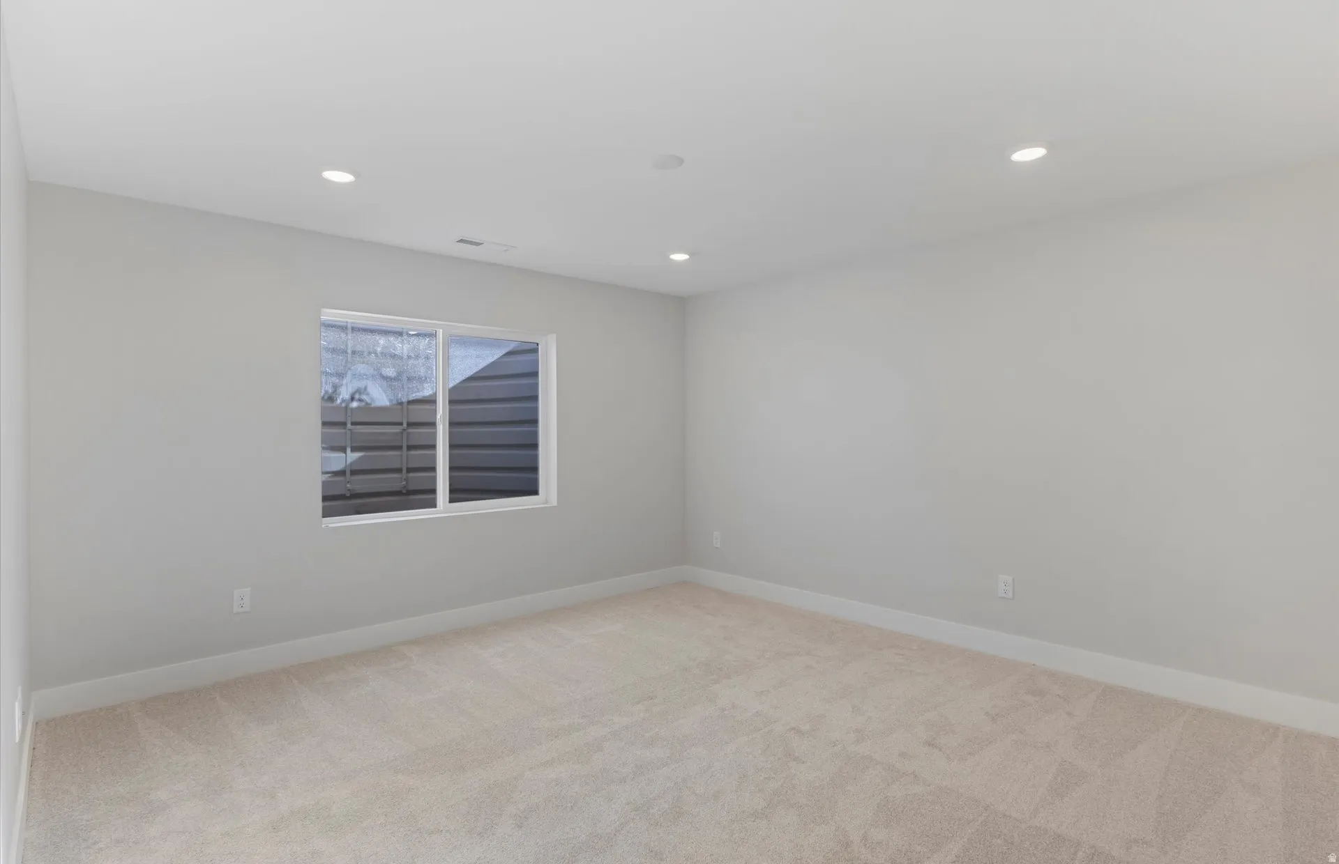 Neutral wall paint, recessed lighting, and light-toned carpet