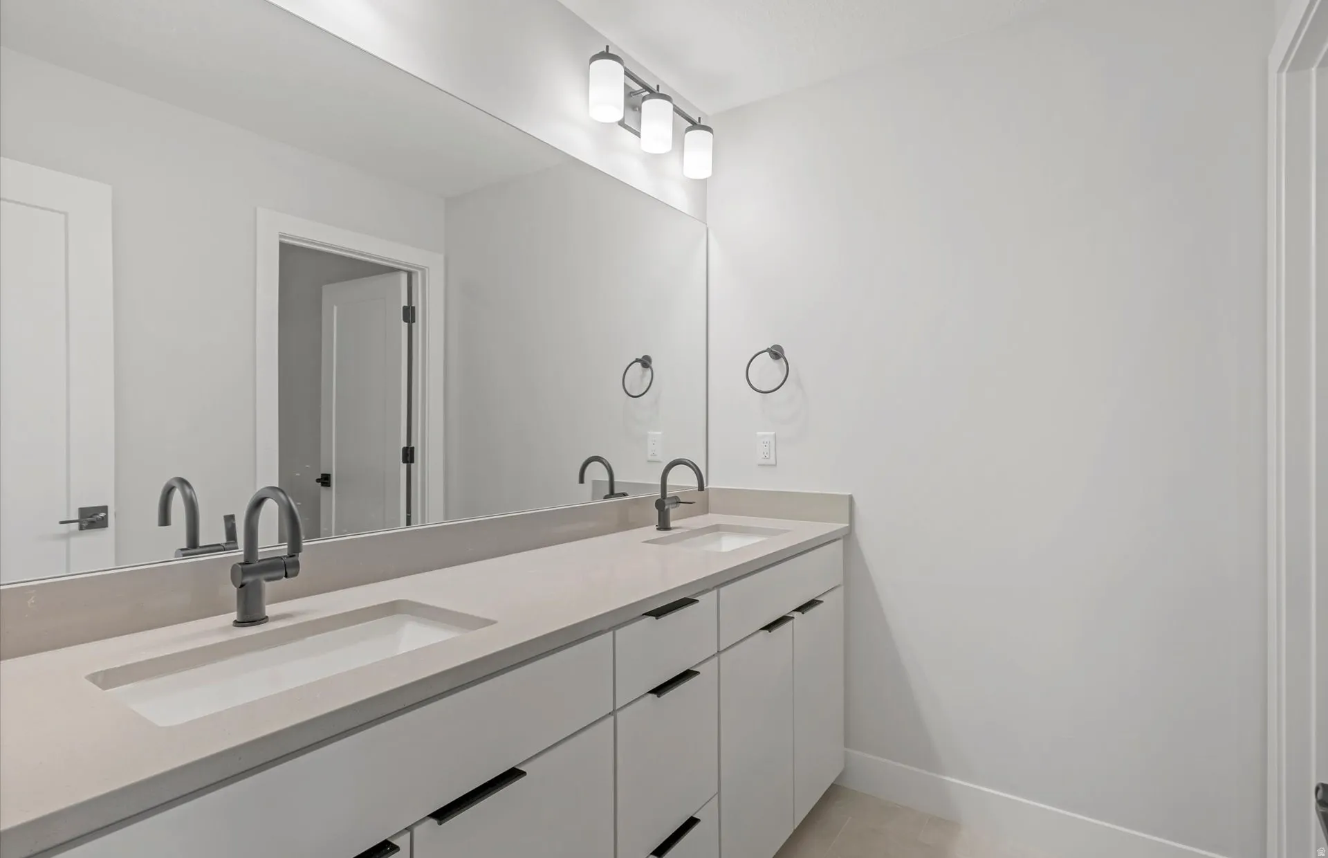 Dual undermount sinks with matte black faucets, integrated countertop, expansive vanity mirror, and modern three-light fixture