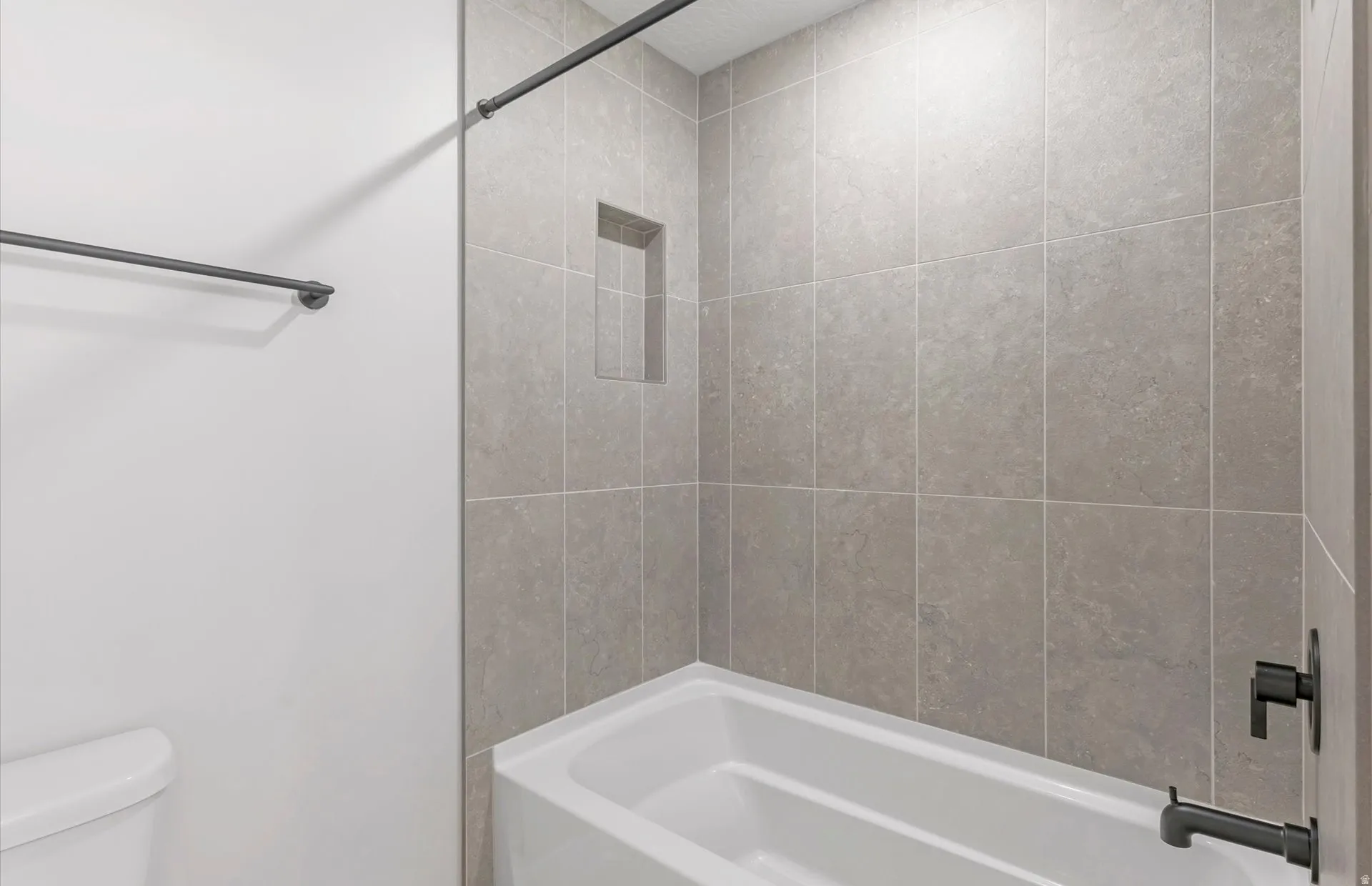 Bathtub with tiled surround, built-in shower niche, and matte black fixtures