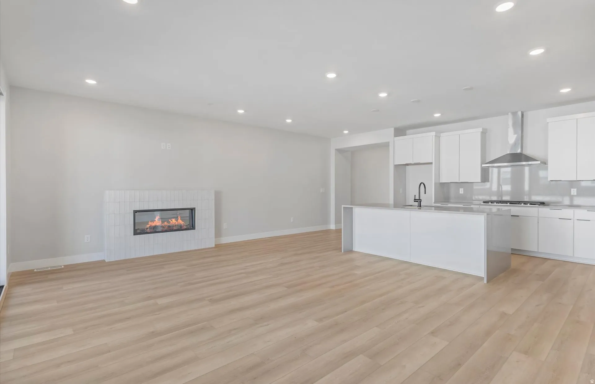 Open-concept living space with wood-finish flooring, recessed lighting, and a modern fireplace with a tiled surround