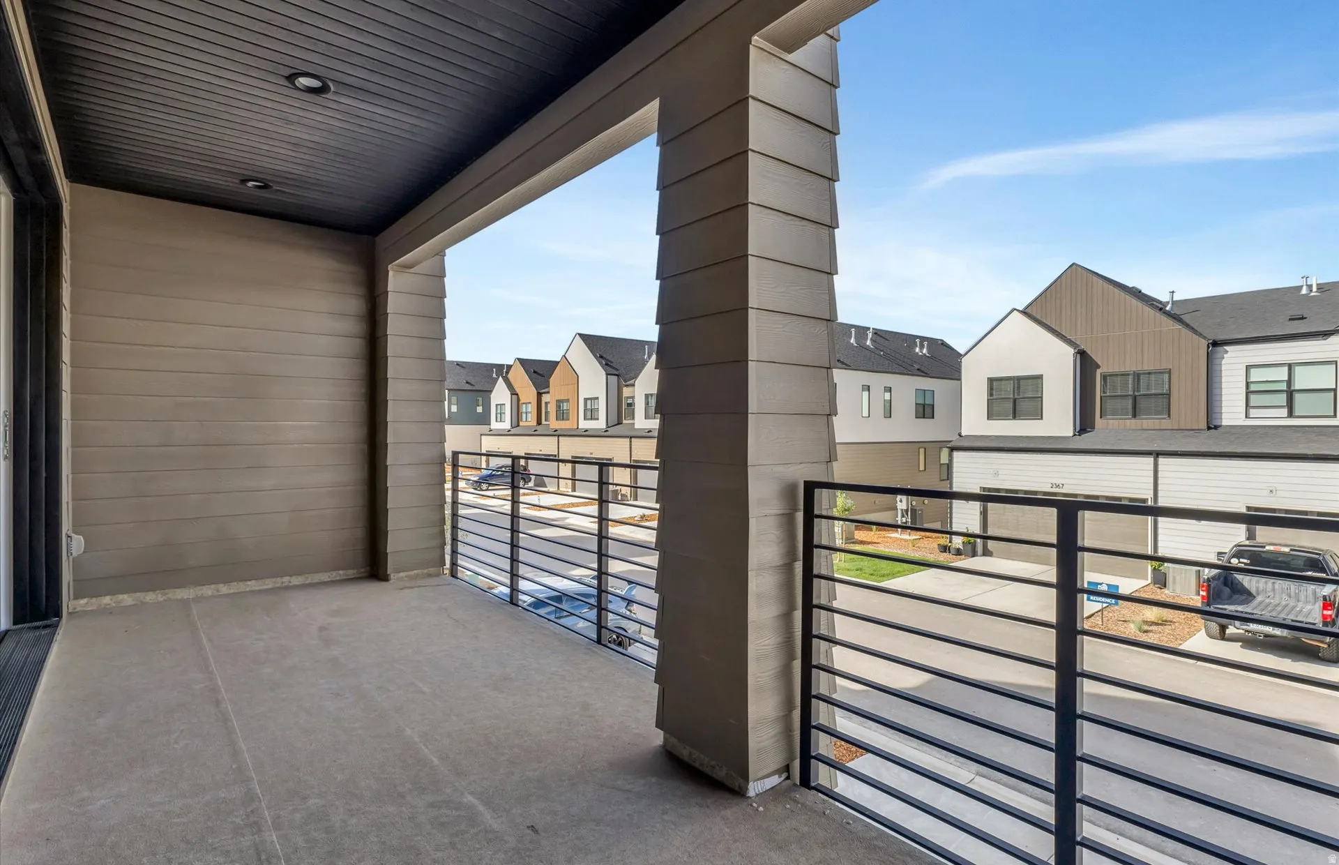 Covered outdoor balcony with a concrete floor, black metal horizontal railings, and recessed ceiling lighting