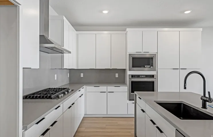 White cabinetry, stainless steel appliances, kitchen island with black sink, light wood-finish flooring, and recessed lighting