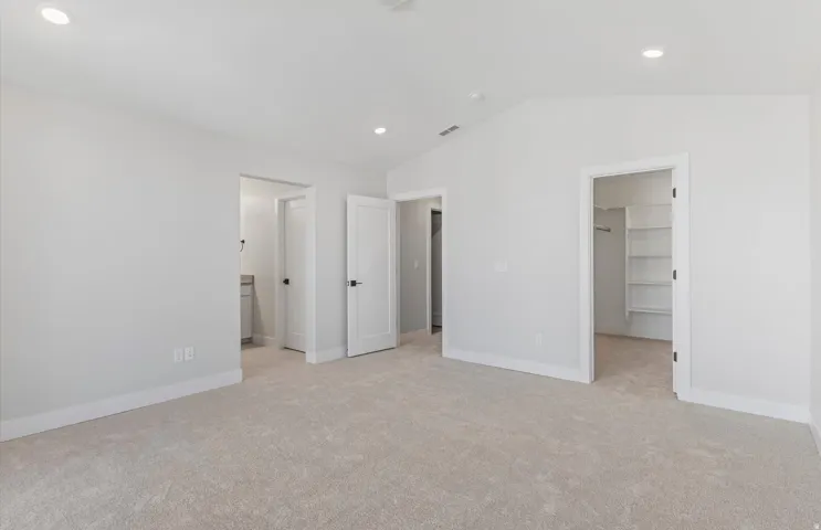 Recessed lighting, vaulted ceiling, light-toned carpeting, built-in closet shelving, and a vanity with a countertop