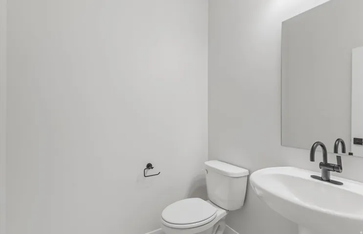 Pedestal sink, matte black faucet, wall-mounted mirror, modern toilet, and white walls